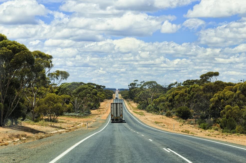 A Truck is Driving Down an Empty Highway Surrounded by Trees — Red Central Towing & Recovery In Alice Springs, N