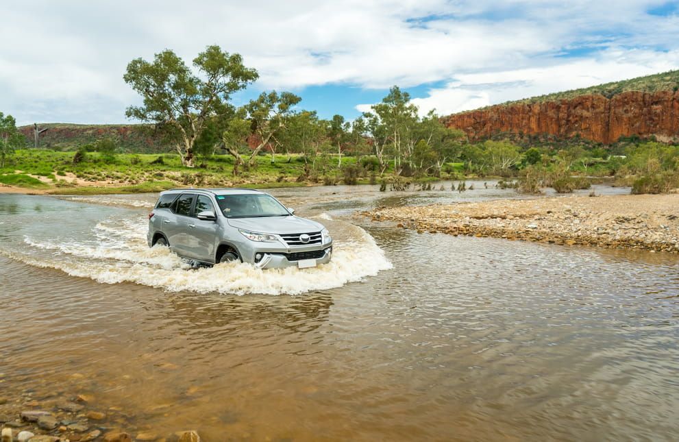 A Car is Driving Through a River on a Dirt Road  — Red Central Towing & Recovery In Alice Springs, N