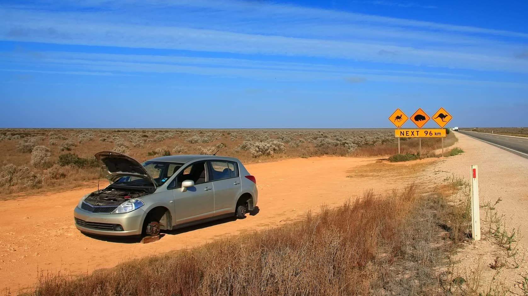A Car With Its Hood Up is Parked on the Side of a Dirt Road — Red Central Towing & Recovery In Alice Springs, NT