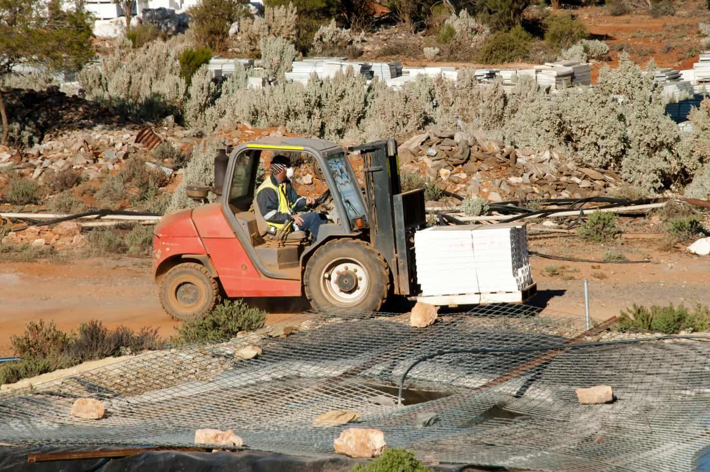A Forklift is Carrying a Pallet of Bricks on a Dirt Road — Red Central Towing & Recovery In Alice Springs, NT