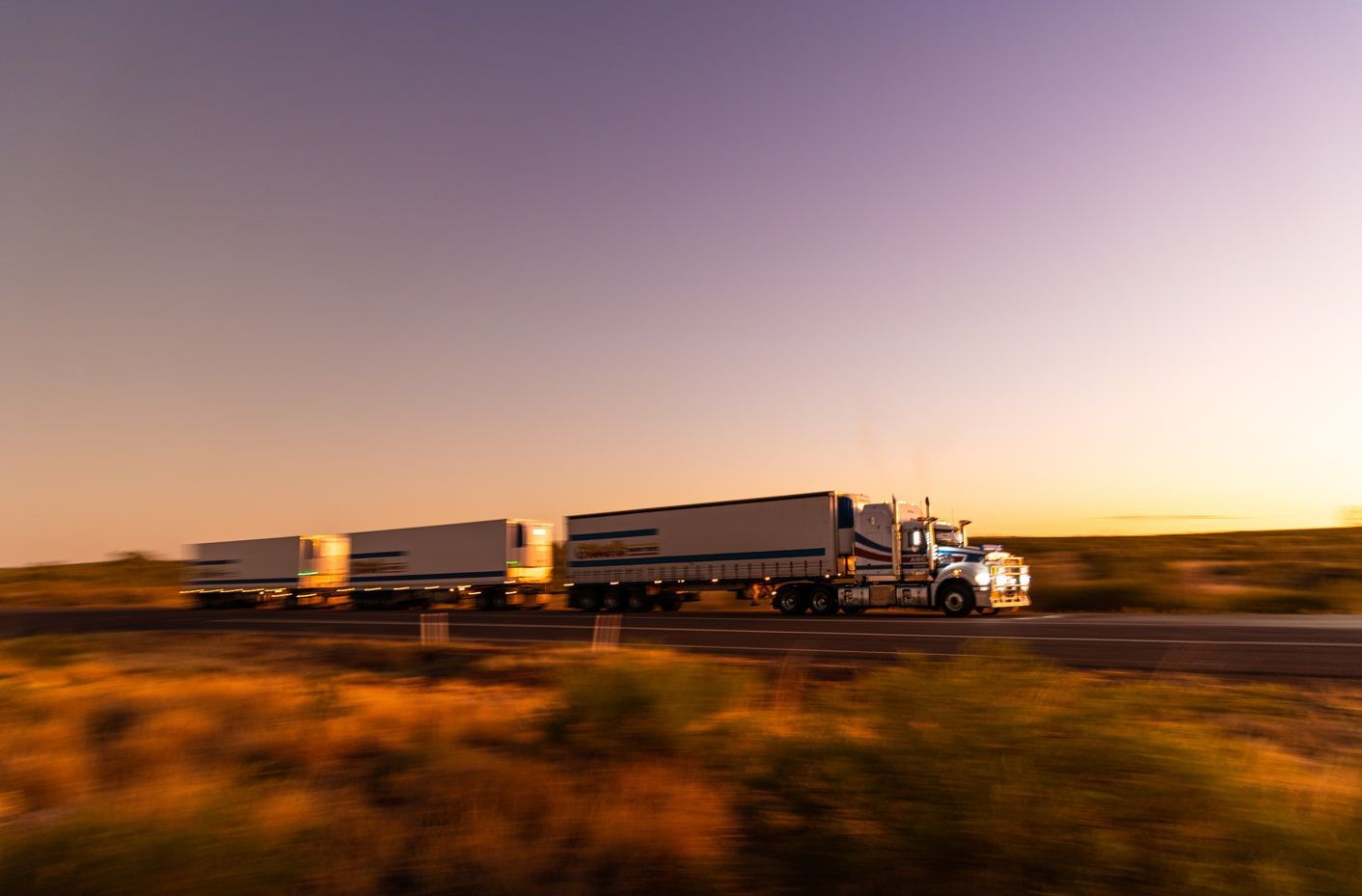 A Semi Truck is Driving Down a Highway at Sunset — Red Central Towing & Recovery In Alice Springs, NT