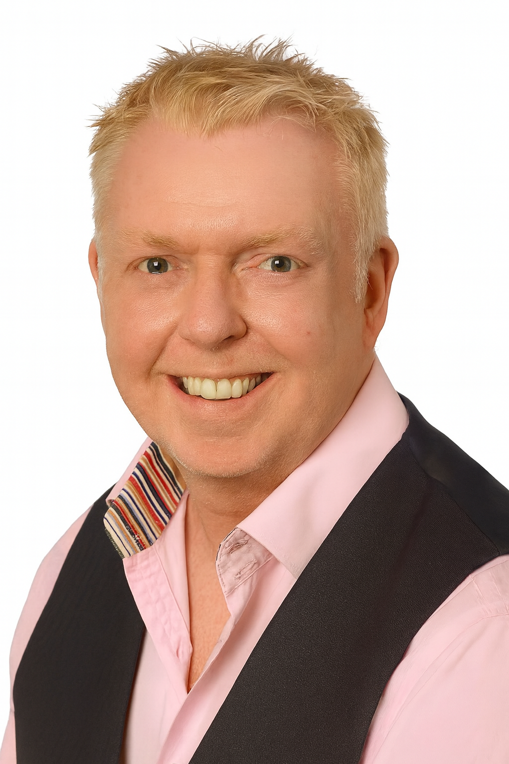 Man with blonde hair smiles, wearing a pink shirt, patterned collar, and black vest.