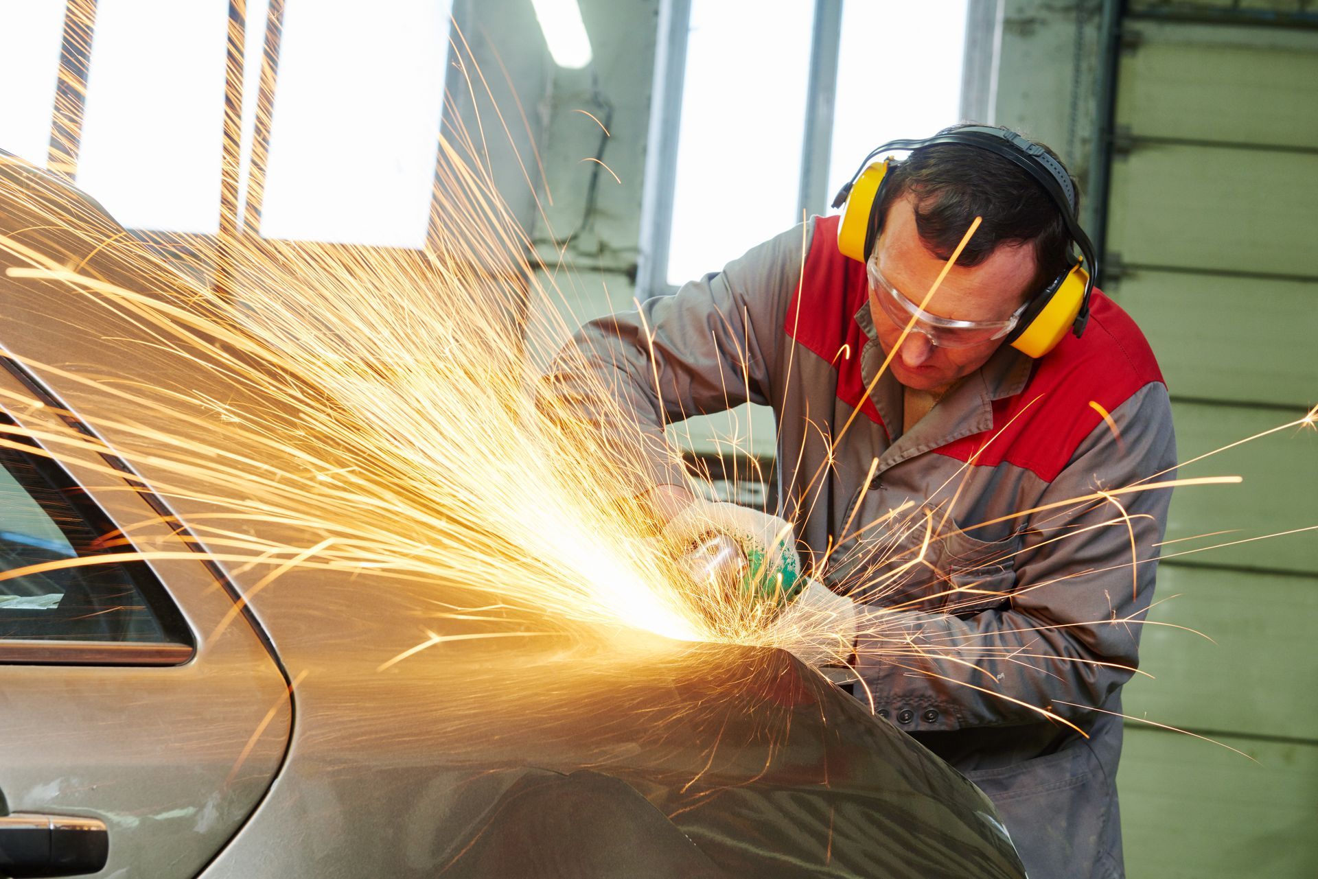Person in protective gear grinding a car, sparks flying.