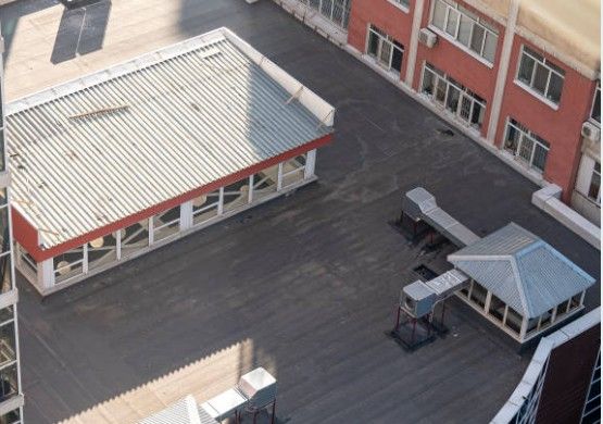 High-angle view of a flat roof with ventilation units and a red-trimmed structure; buildings in the background.