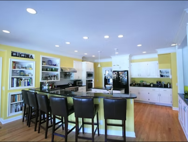 Kitchen with yellow walls, white cabinets, black countertop, and bar stools.