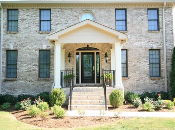 Brick house with a covered entryway, featuring steps and a black front door.