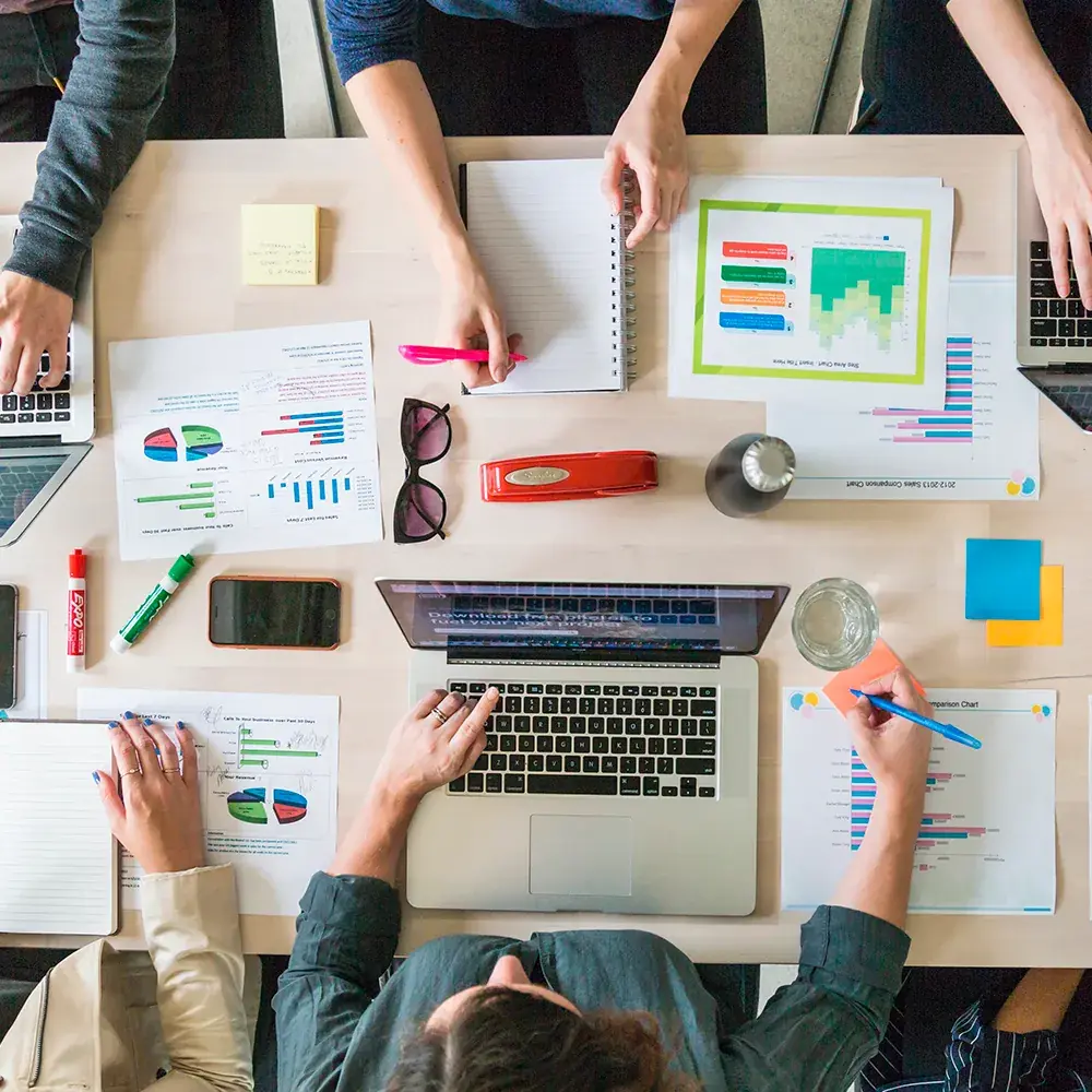 Mesa de reunião de negócios com notebook, gráficos impressos e anotações.