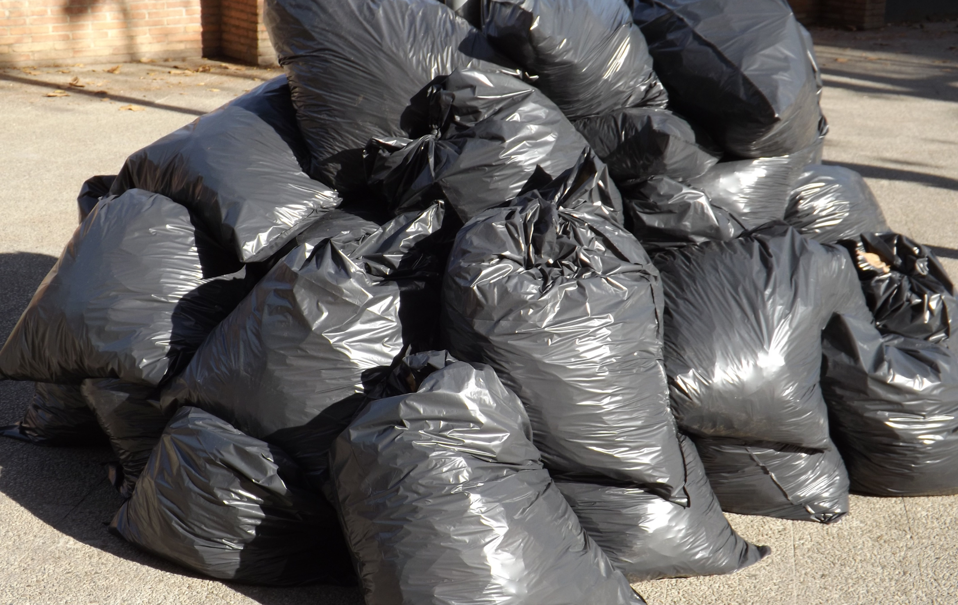 A pile of black garbage bags are stacked on top of each other on the ground.