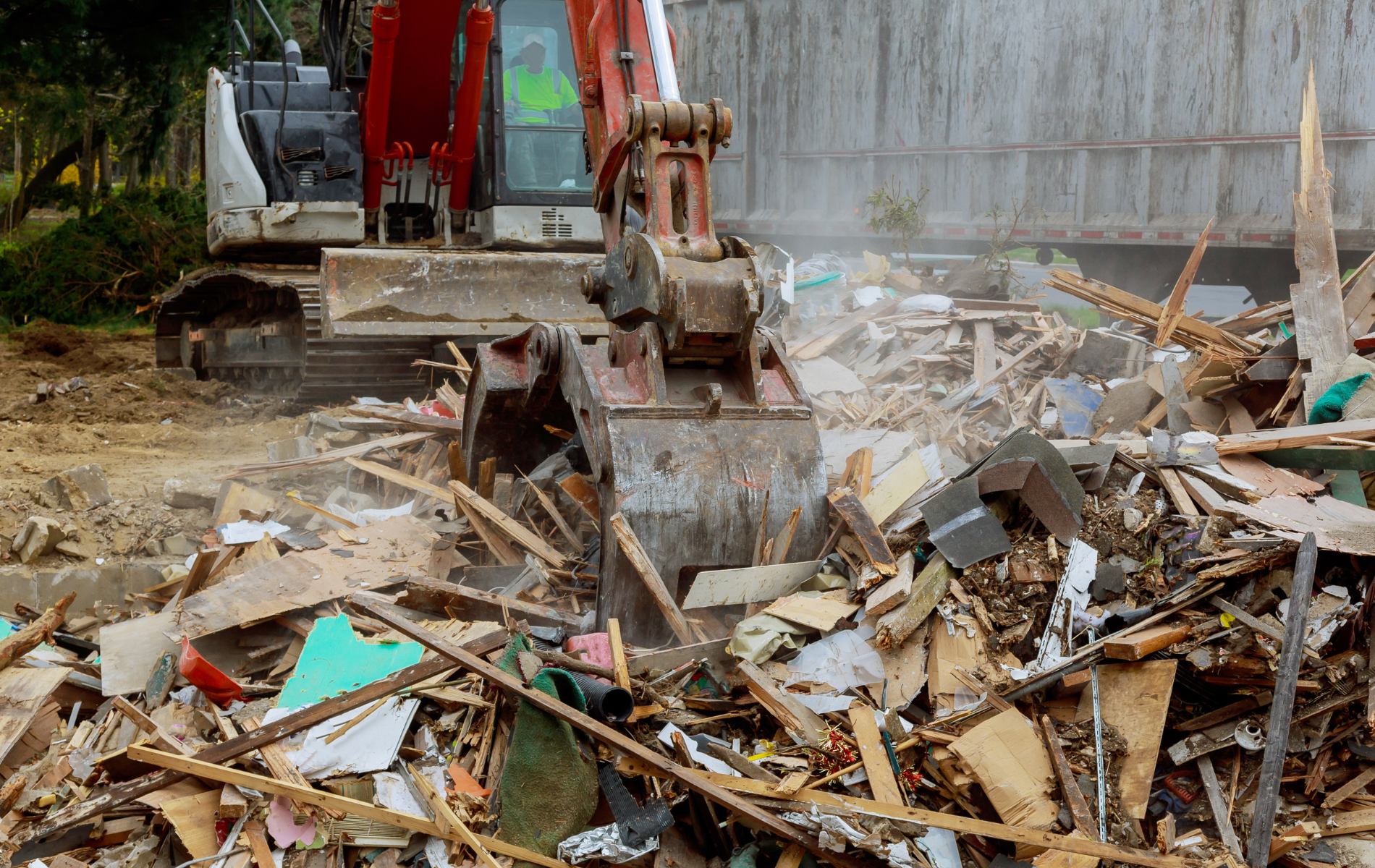A bulldozer is demolishing a building with a pile of wood in the foreground.