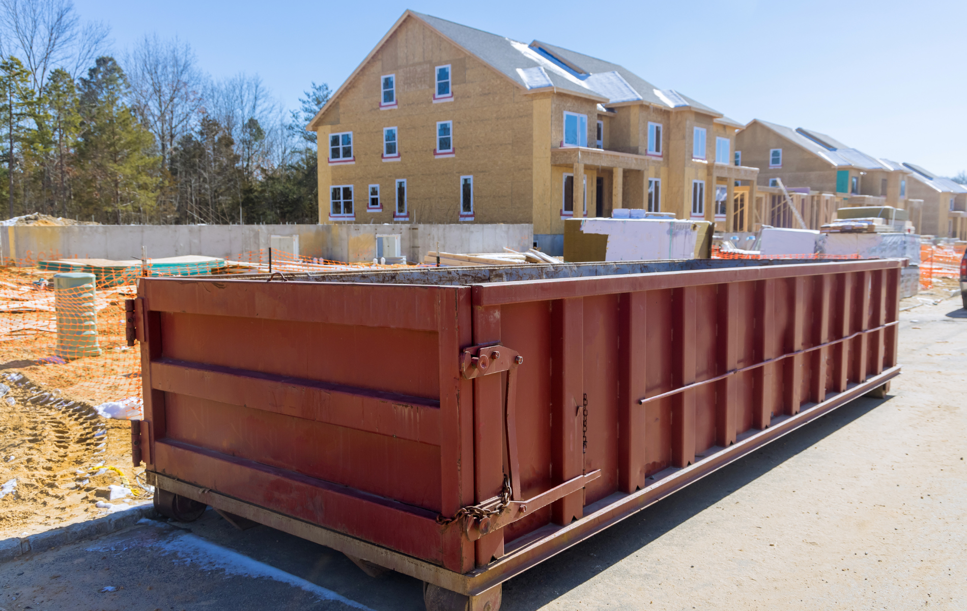 A large dumpster is parked in front of a building under construction.