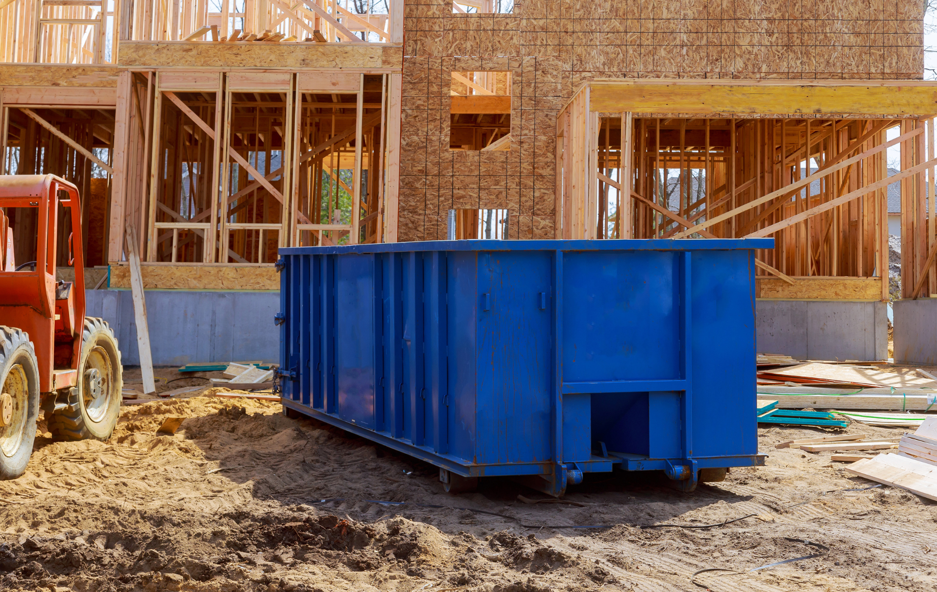 A blue dumpster is parked in front of a house under construction.