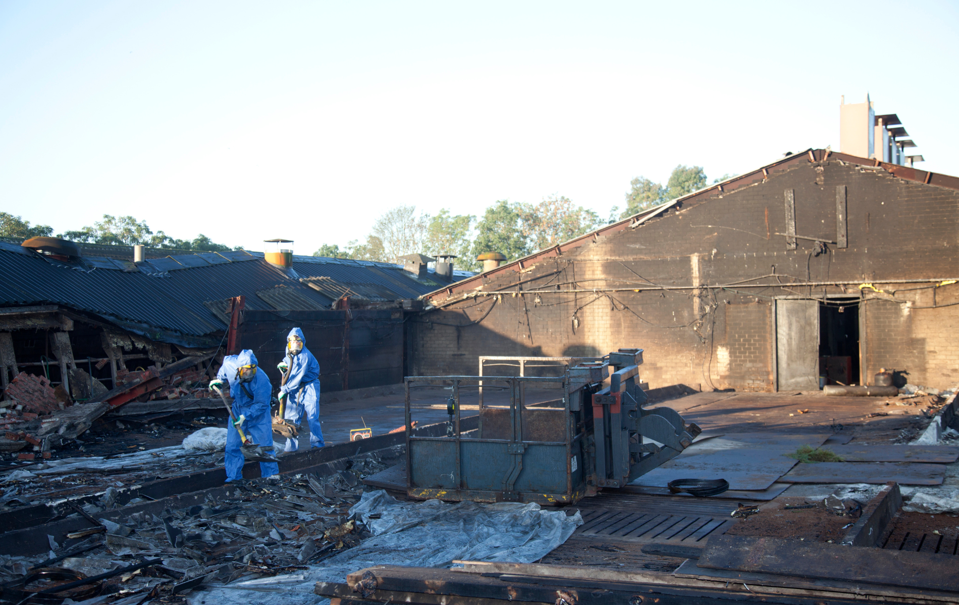 Workers in protective suits clean up a burned-down building.
