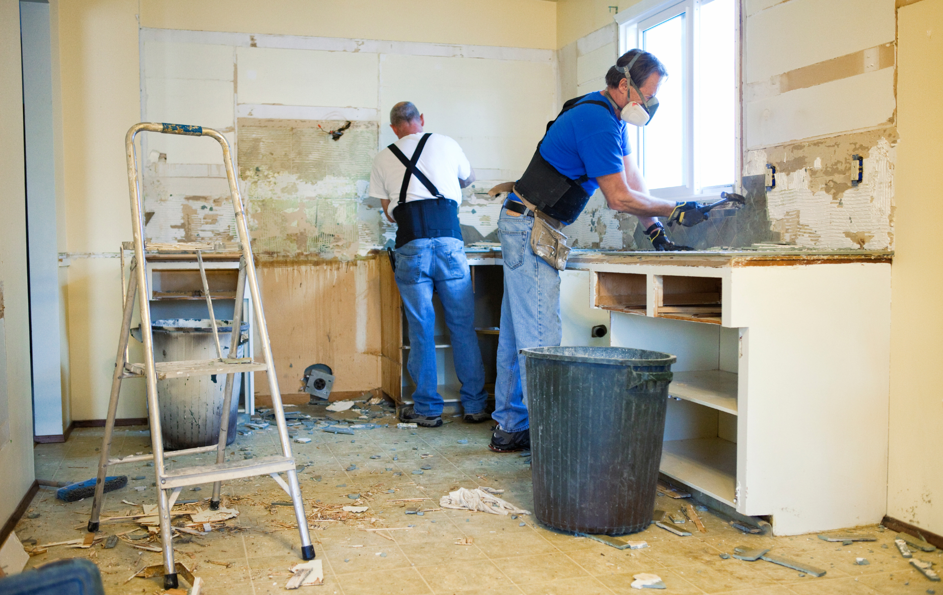 Two men are cleaning a kitchen with a bucket and a ladder.