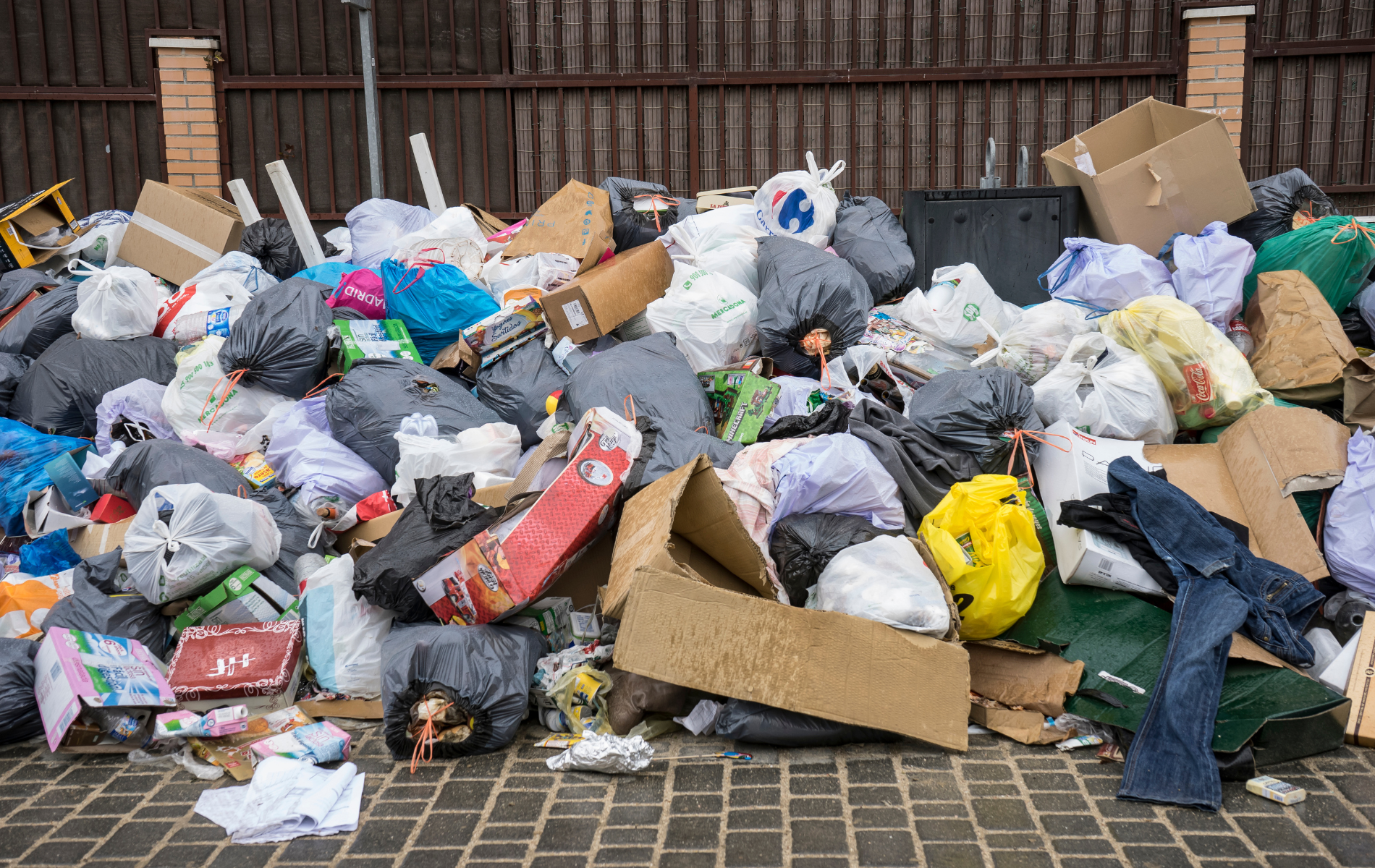 A pile of garbage is sitting on the sidewalk in front of a fence.