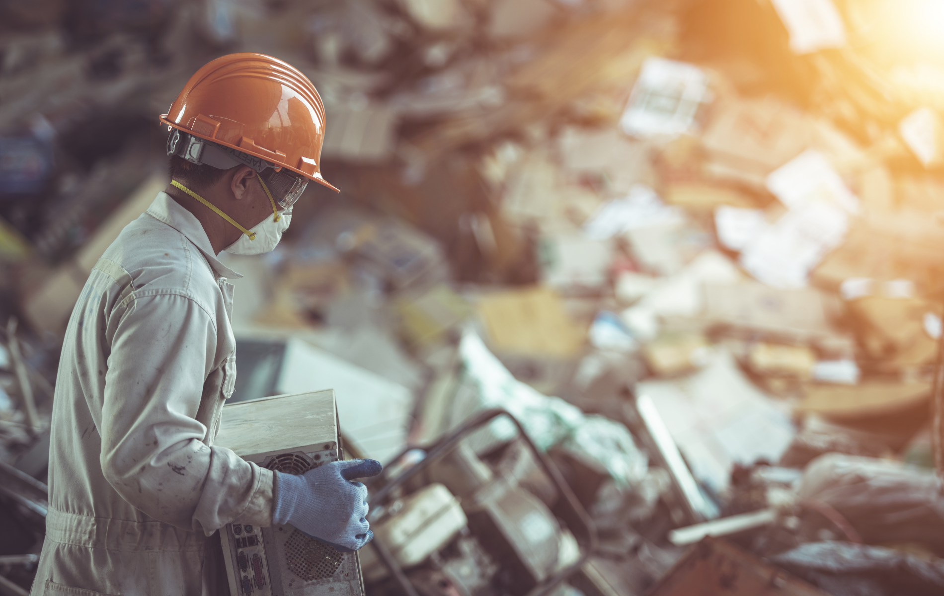 A man wearing a hard hat , mask and gloves is standing in front of a pile of trash.