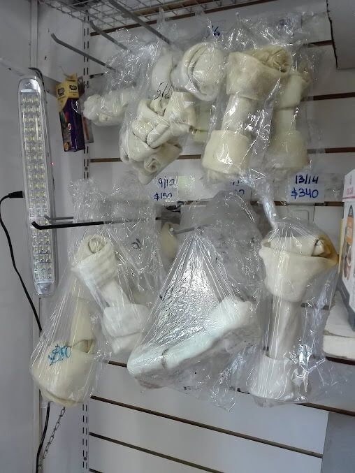 Varios huesos de perro de cuero crudo, blancos y anudados, envueltos en envases de plástico transparente, cuelgan en la pared de un escaparate.