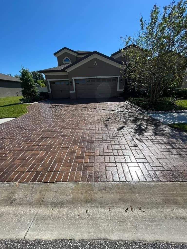 Brick-patterned driveway in front of a two-story house with a blue sky.