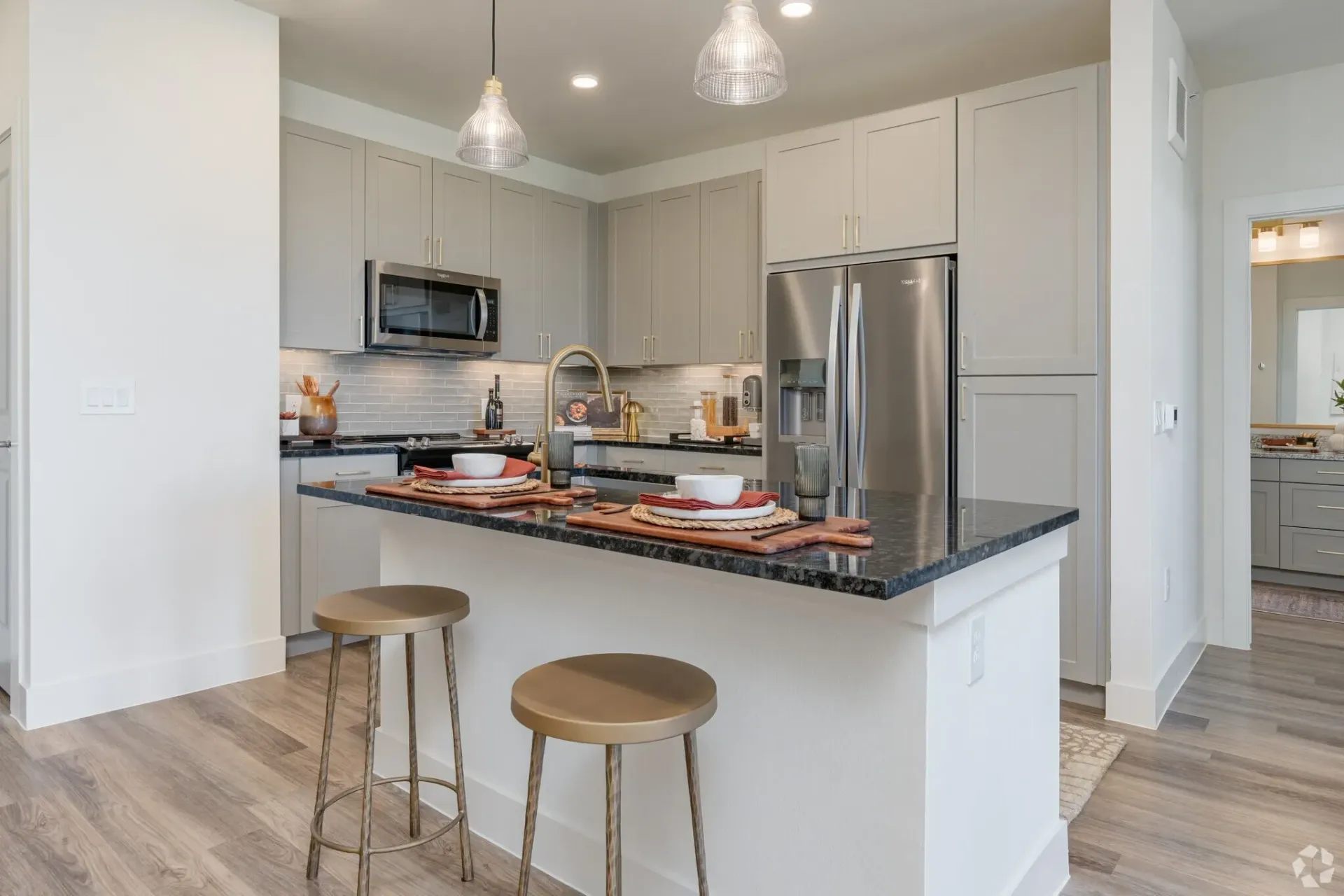 Modern kitchen with light gray cabinets, stainless steel appliances, a black granite island, and two stools.