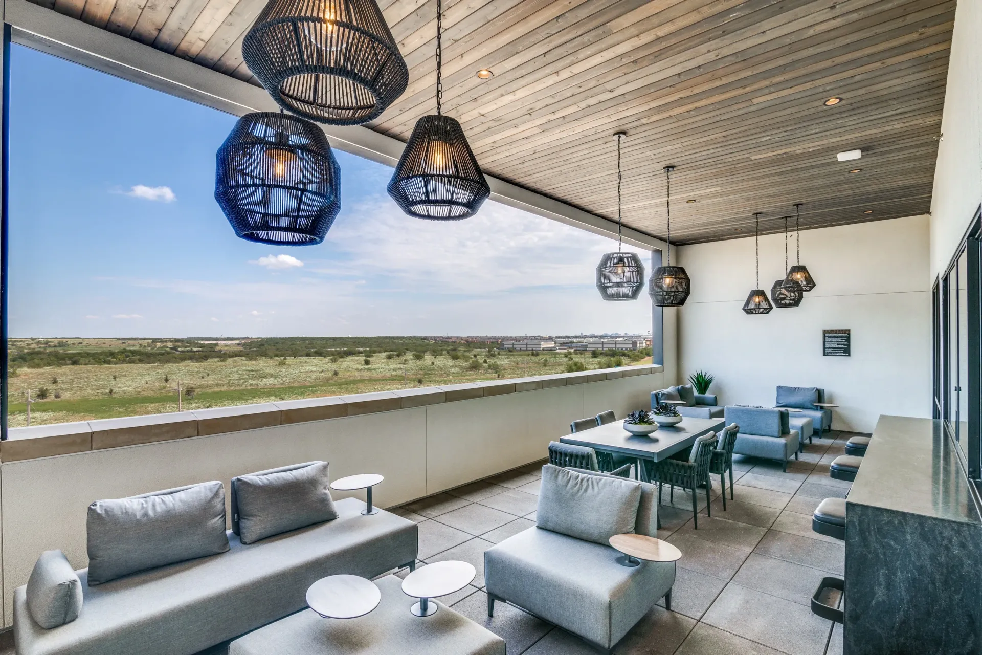 Spacious covered balcony with modern lounge furniture, dining table, and scenic views.