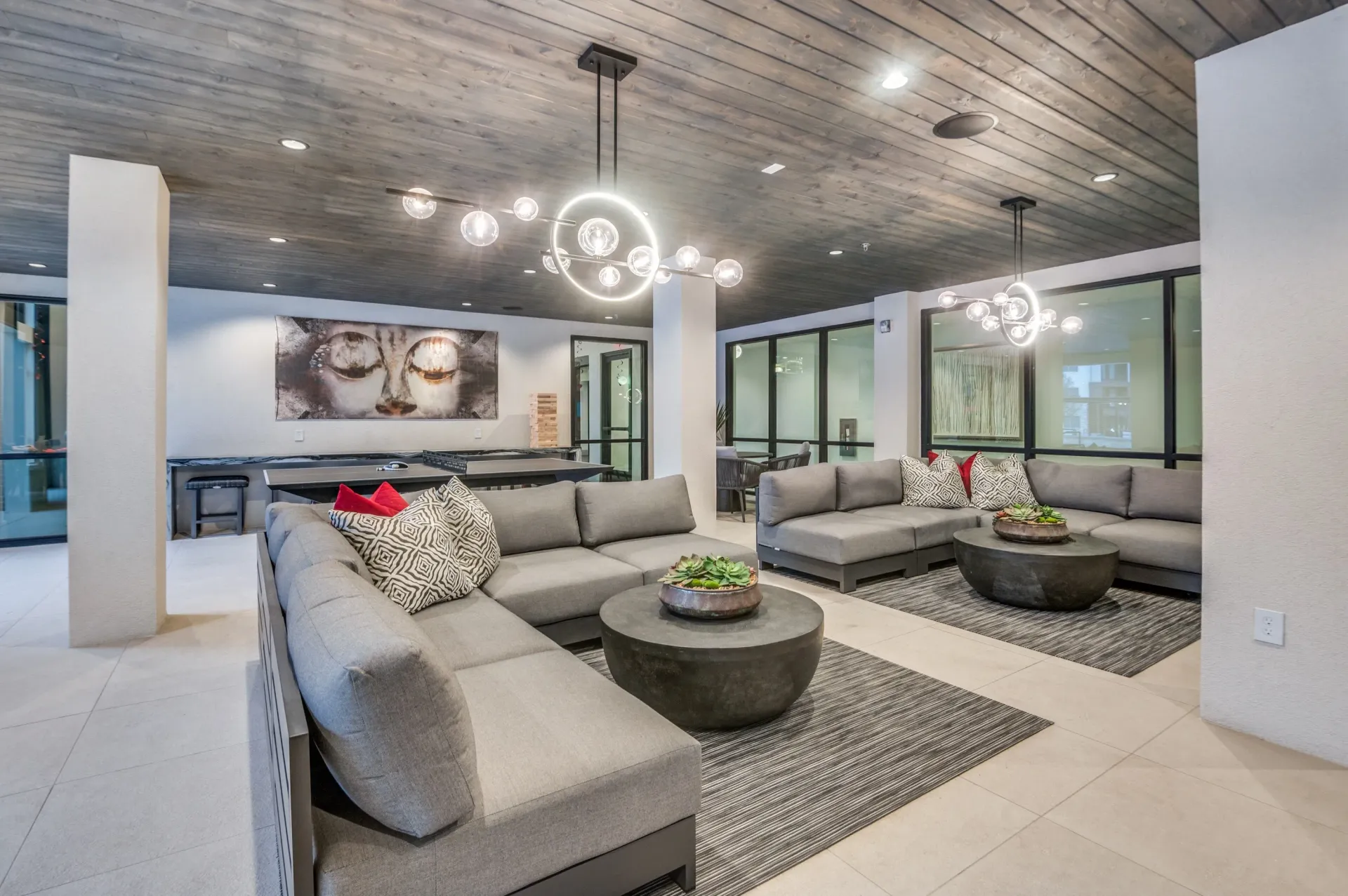 Modern lounge area with large grey sectional sofas, round coffee tables, and abstract art on the wall.