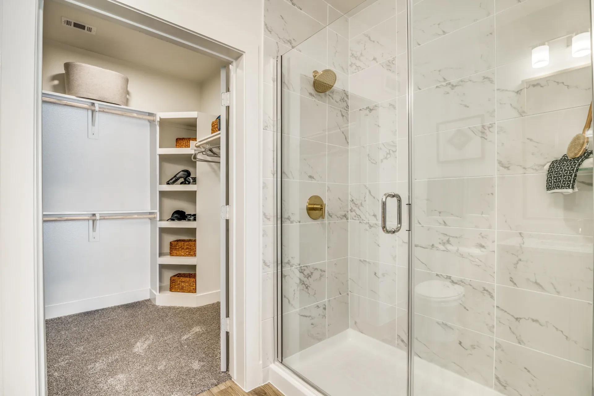 Walk-in closet and glass-enclosed shower with marble tile and gold fixtures.