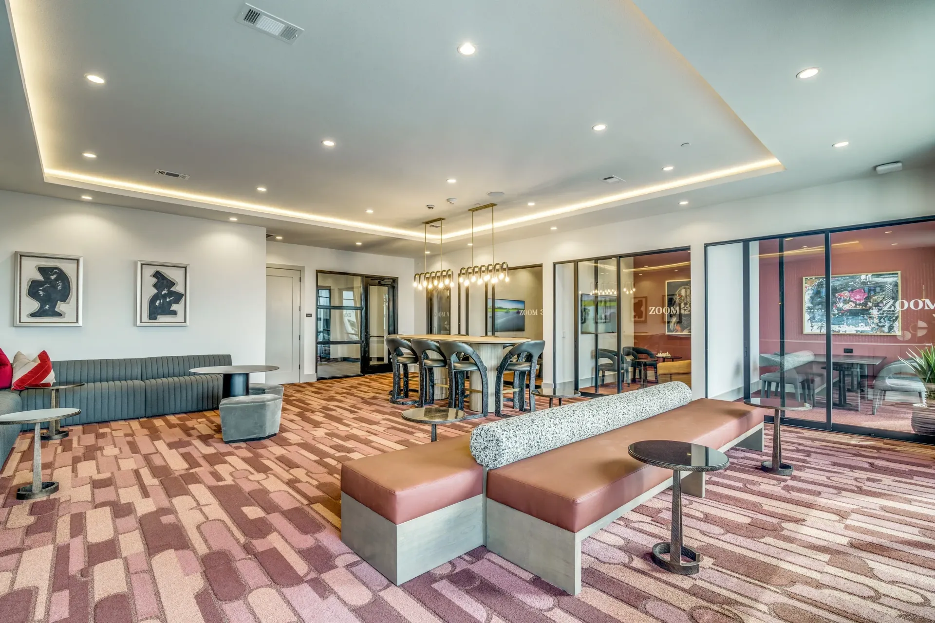Modern lounge area with comfortable seating, a communal table, and glass-enclosed rooms.