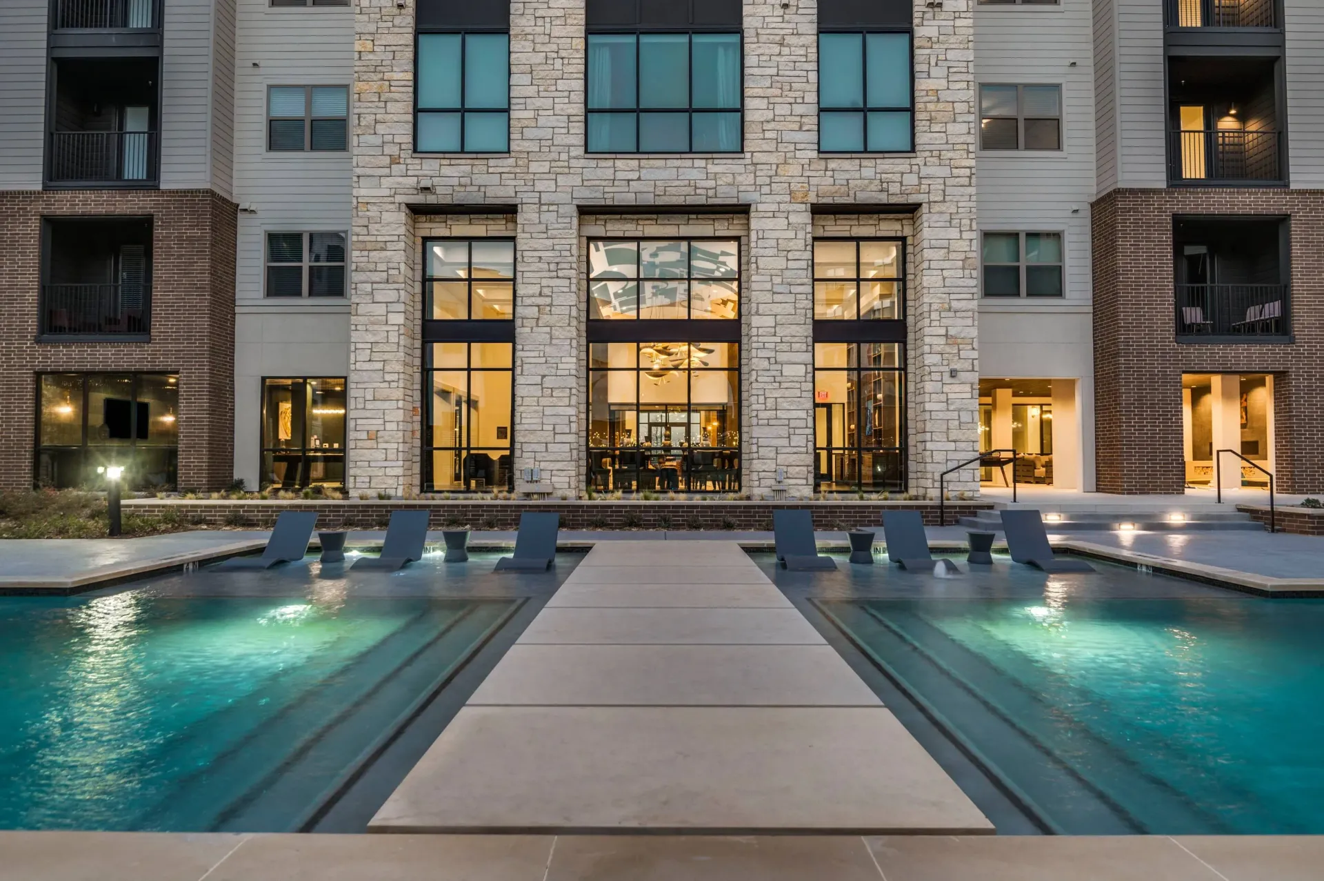 Modern apartment building exterior with an infinity pool and lounge chairs.