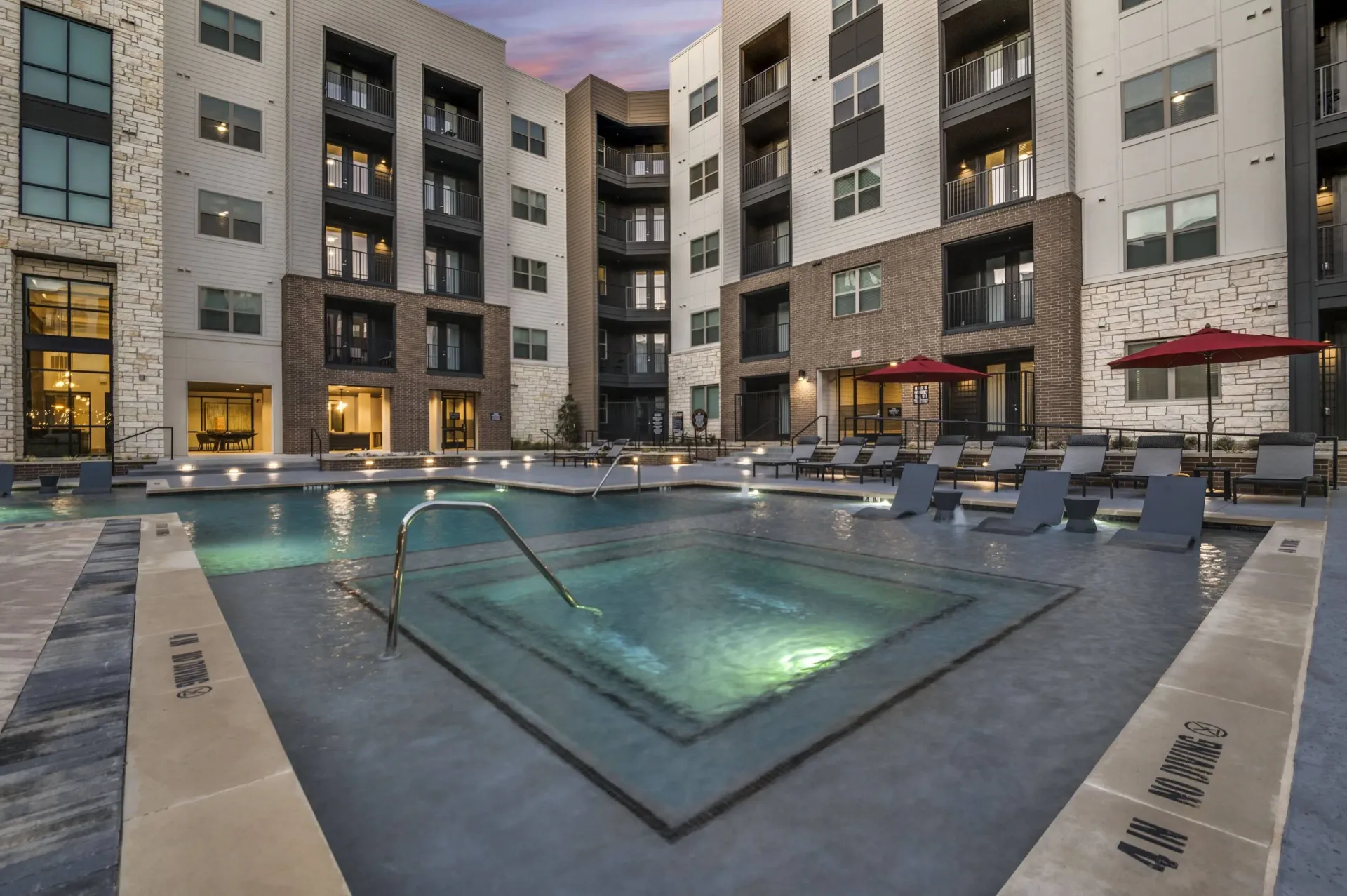 Resort-style pool and spa area with lounge chairs at a modern apartment building.