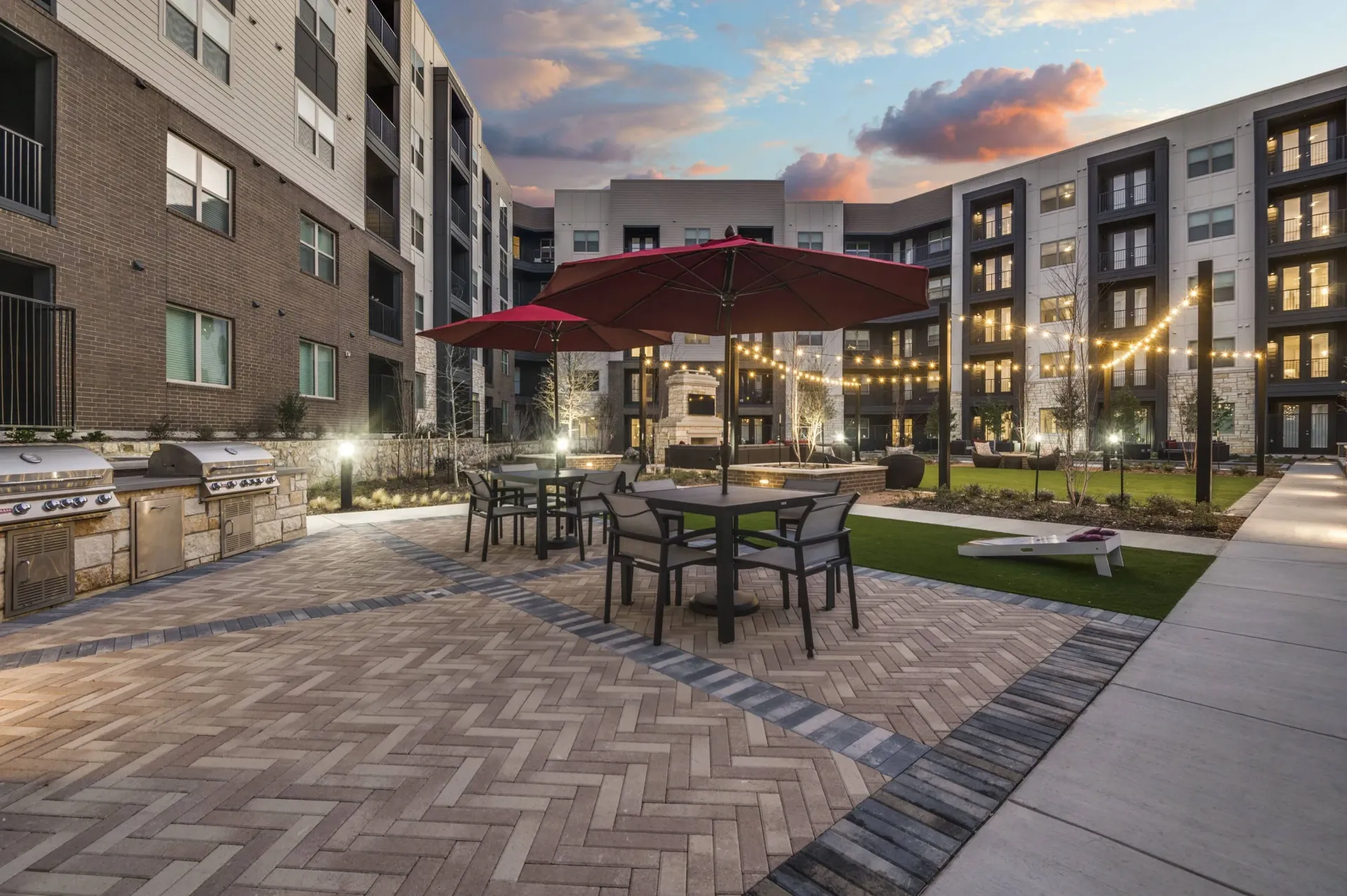 Outdoor courtyard with grills, tables, umbrellas, fire pit, and string lights.