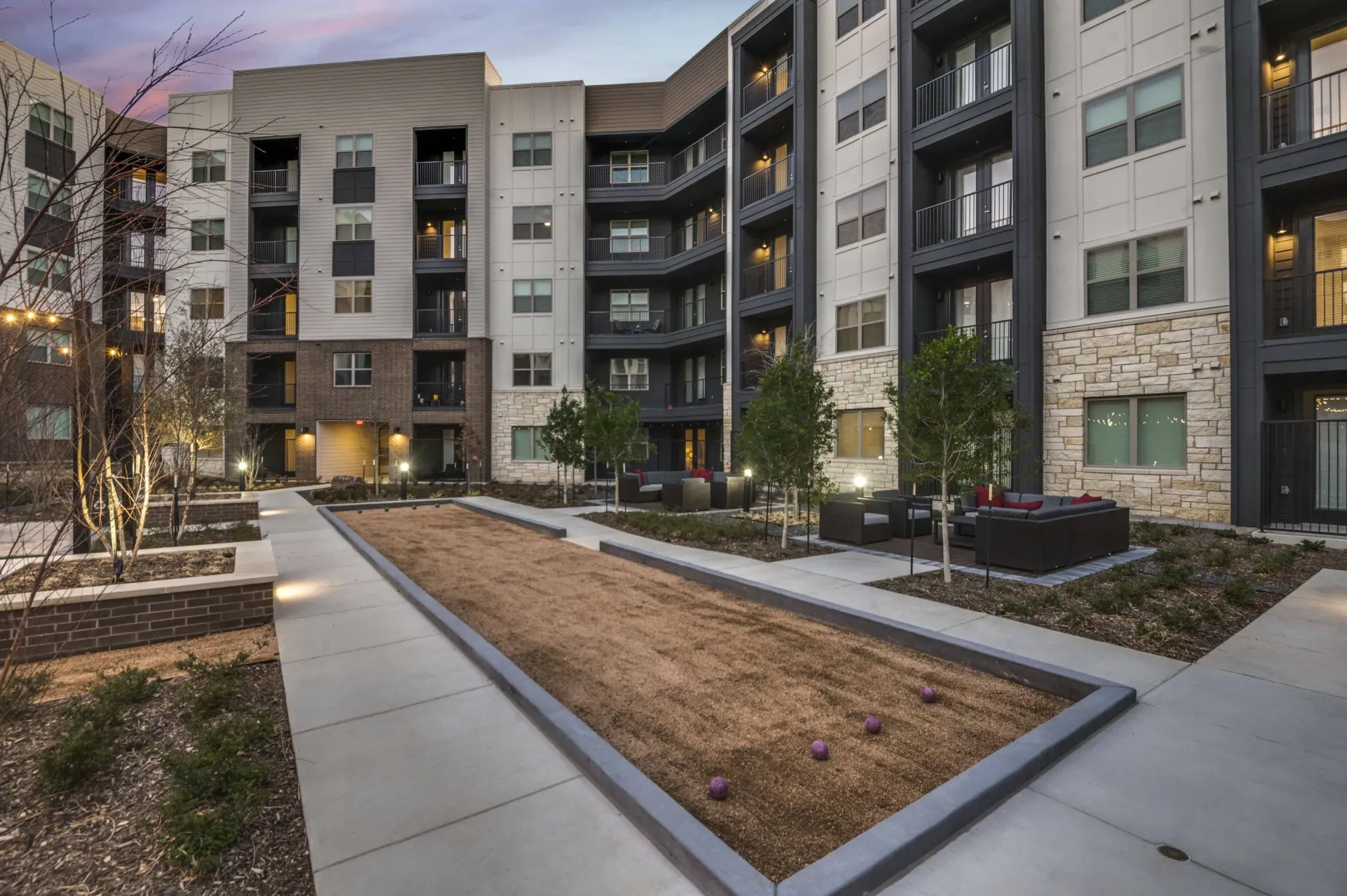 Outdoor bocce ball court and seating area in a modern apartment complex courtyard.