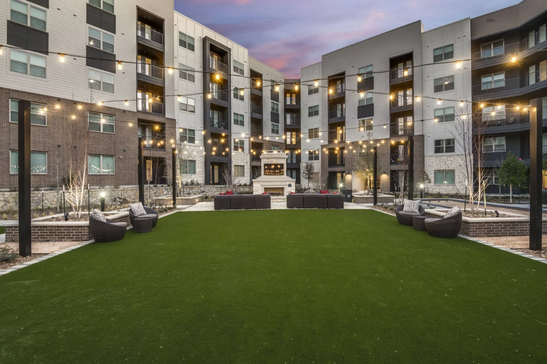 Courtyard with outdoor fireplace, seating areas, and string lights.