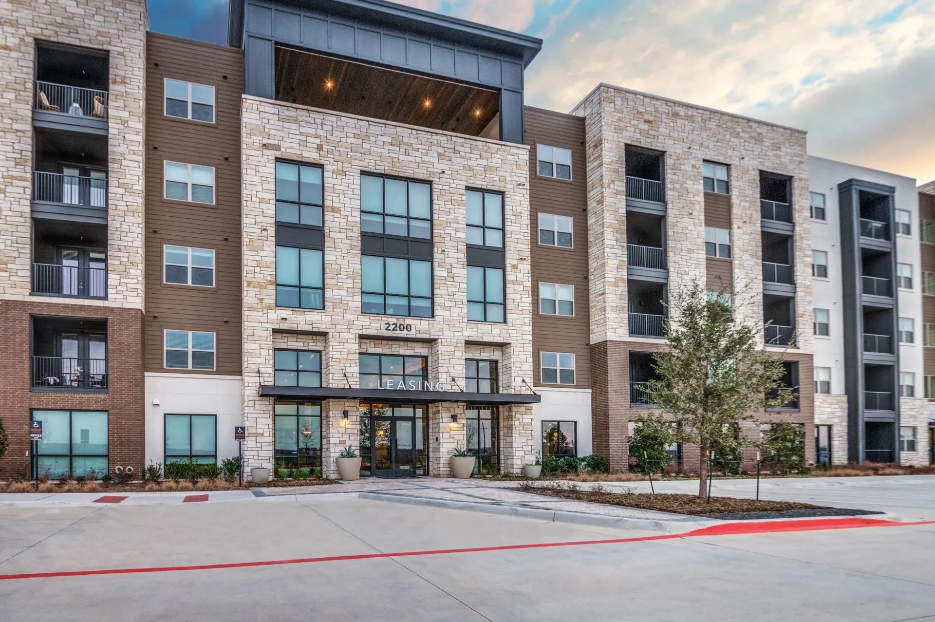 Exterior view of a modern apartment building with stone and brown siding, featuring balconies and a leasing entrance.
