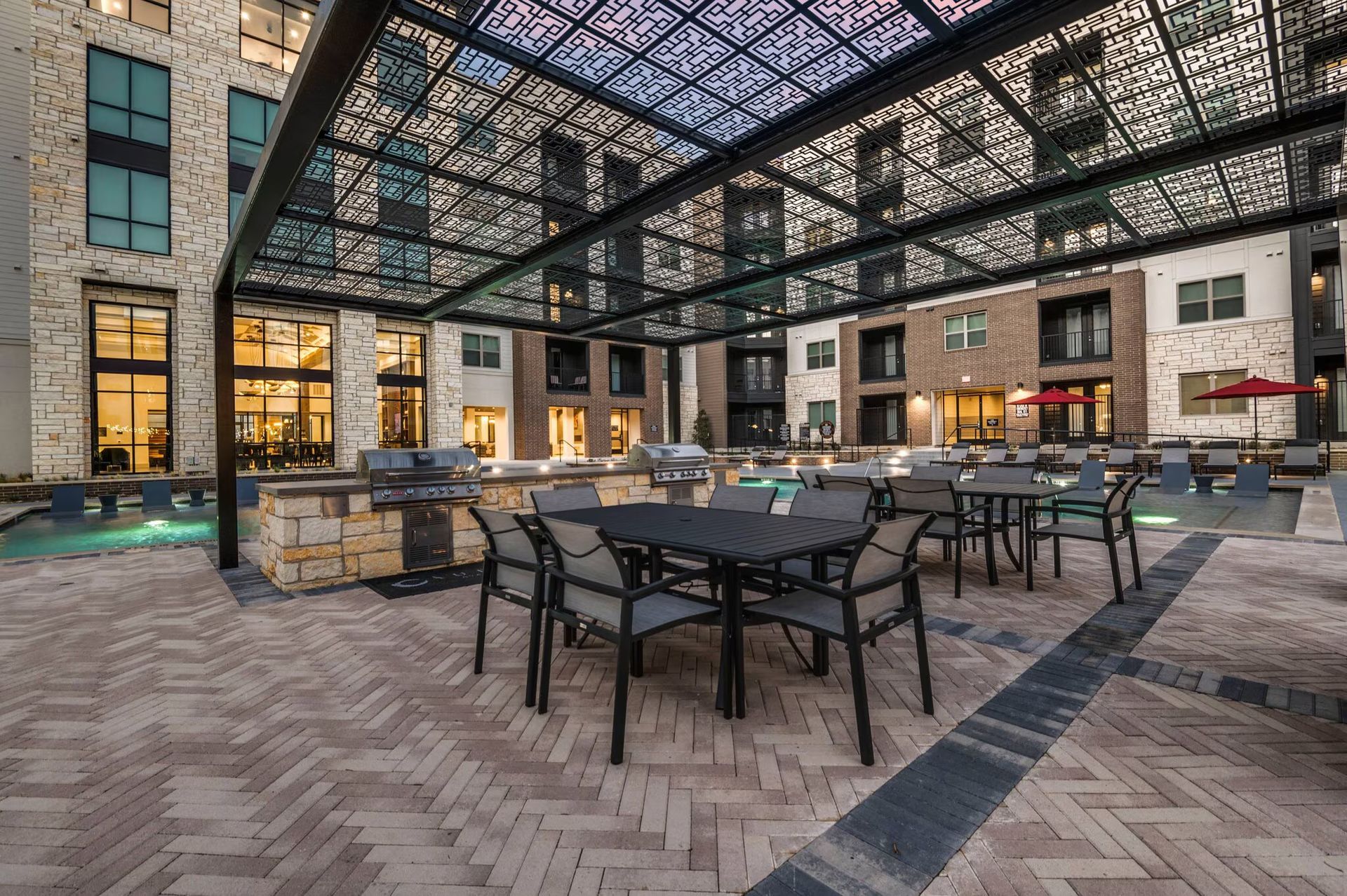 Indoor courtyard patio with tables and chairs under a glass roof, surrounded by brick buildings at dusk