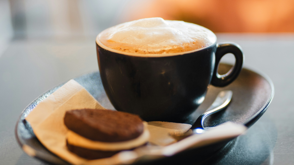 Black cup of coffee on a saucer with a spoon and cookie on a napkin