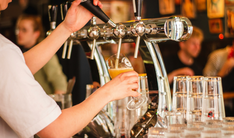 Bartender pouring beer from a tap into a glass beside a row of filled glasses in a lively bar.