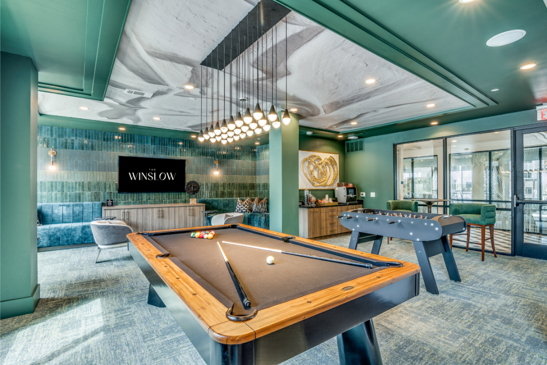 A recreation room with a pool table, a foosball table, modern green walls, and decorative ceiling lighting.