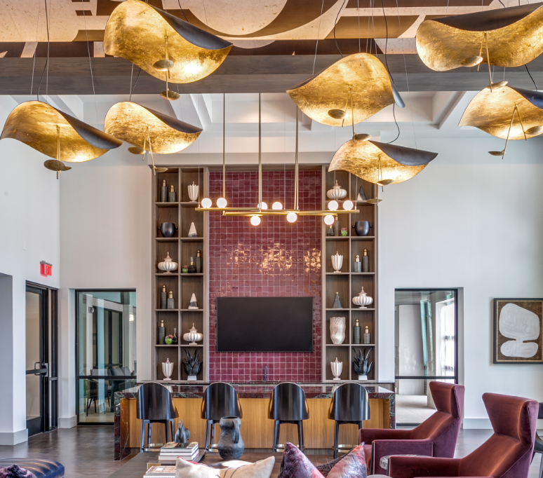 Modern lobby with gold pendant lights, bar shelving, and a wall-mounted TV behind a seating area