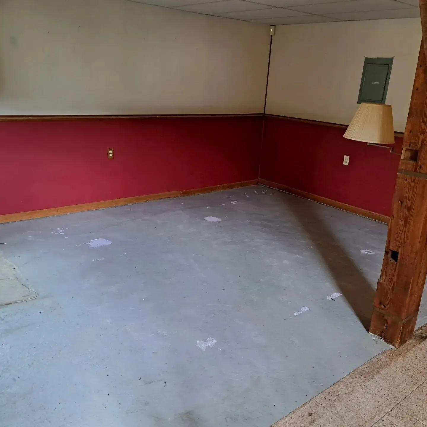 Empty room with red wainscoting and white upper walls, gray floor, bare light fixture, and wooden post.
