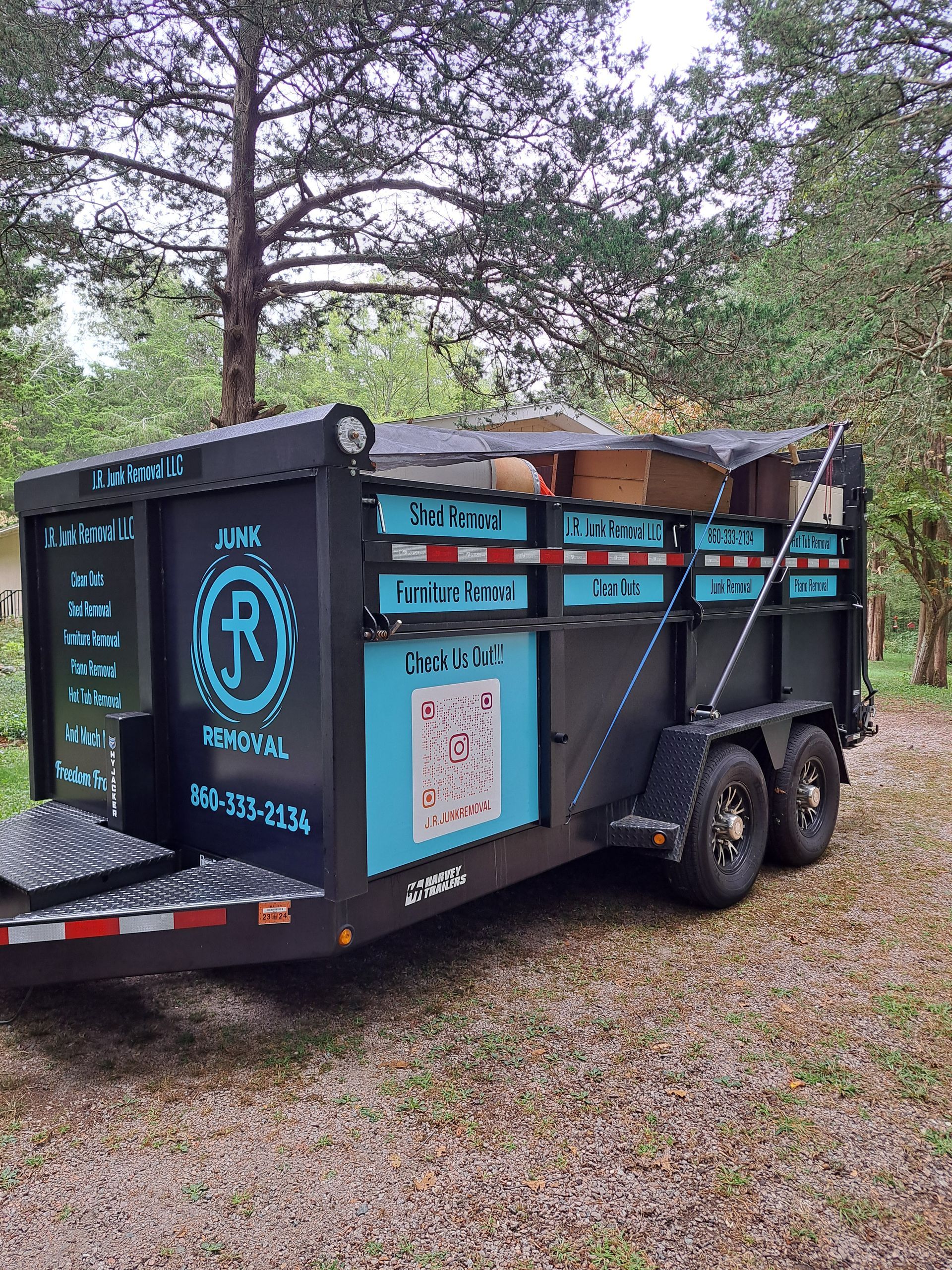 A black and teal junk removal trailer is parked outside, loaded with items, text and logo on the side.