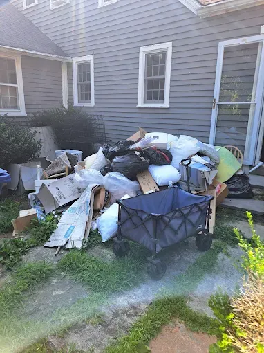 A large pile of trash and cardboard next to a house, including a blue wagon.