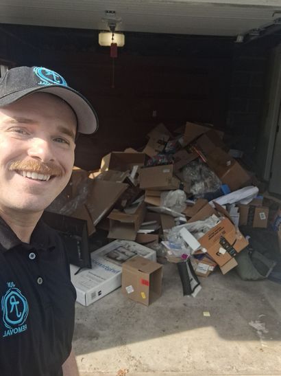 Pile of boxes, bags, and items sits in a garage. Contains trash bags, boxes, a car, and sports equipment.