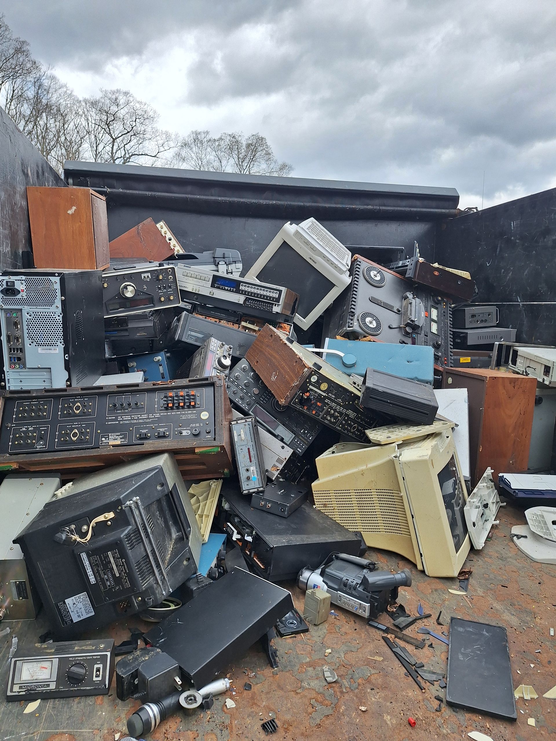 Piled scrap electronics and broken computer parts outdoors under a cloudy sky