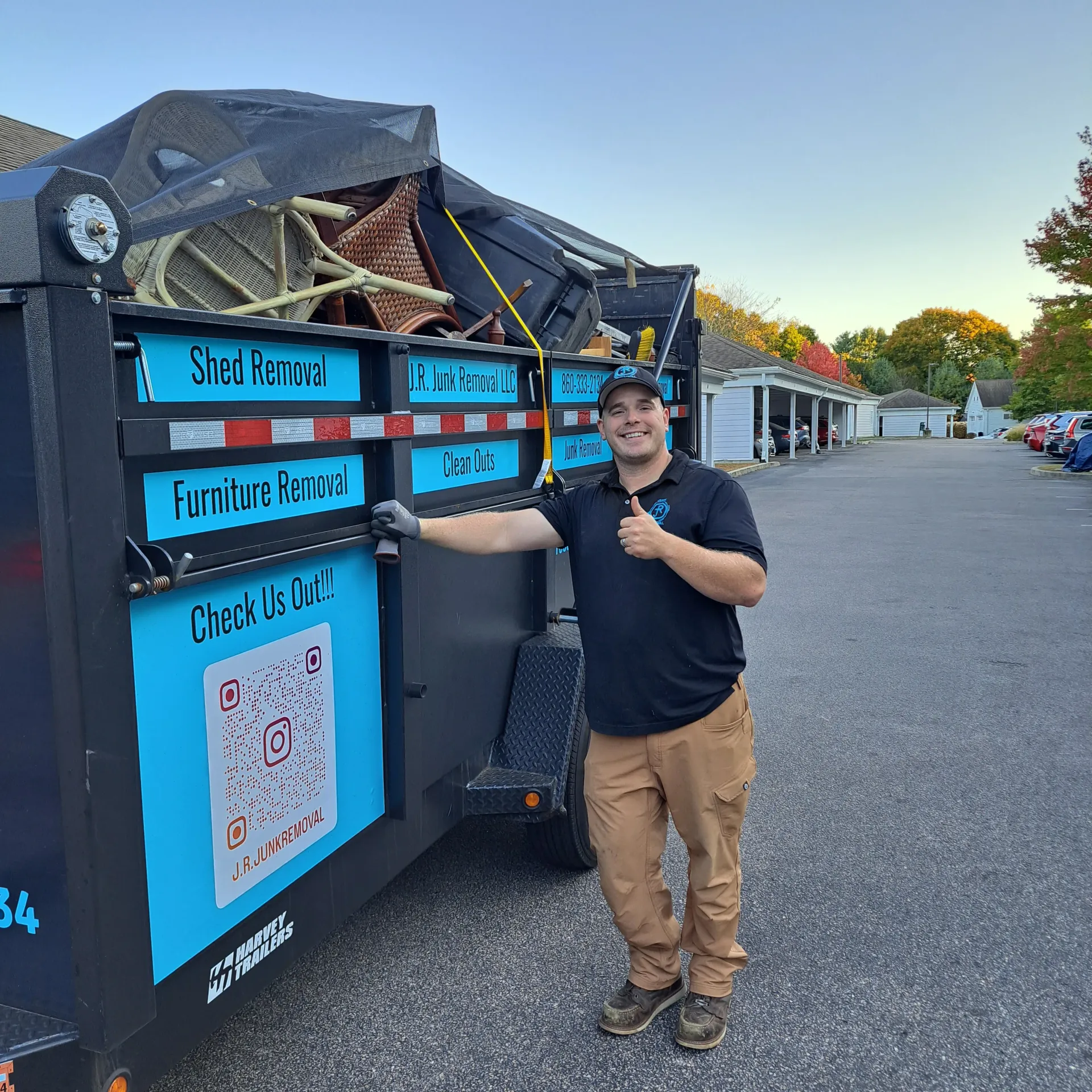 Man standing by a dumpster trailer, giving a thumbs up. The trailer has text for junk removal services.