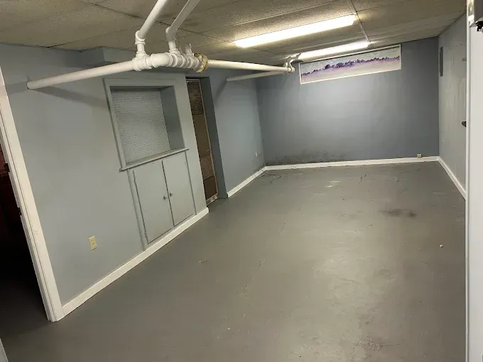 Gray basement room with painted walls, cabinets, pipes, and fluorescent lighting.
