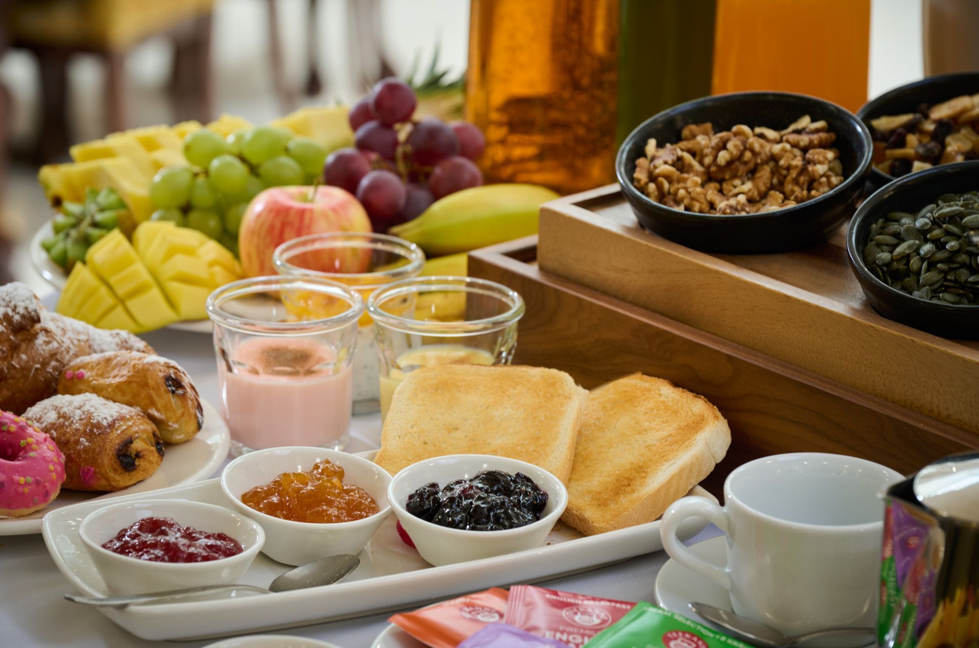 Frühstücksbuffet mit reichhaltigem Angebot: Obst, Gebäck, Joghurt, Toast, Nüsse, Marmeladen und Getränke.