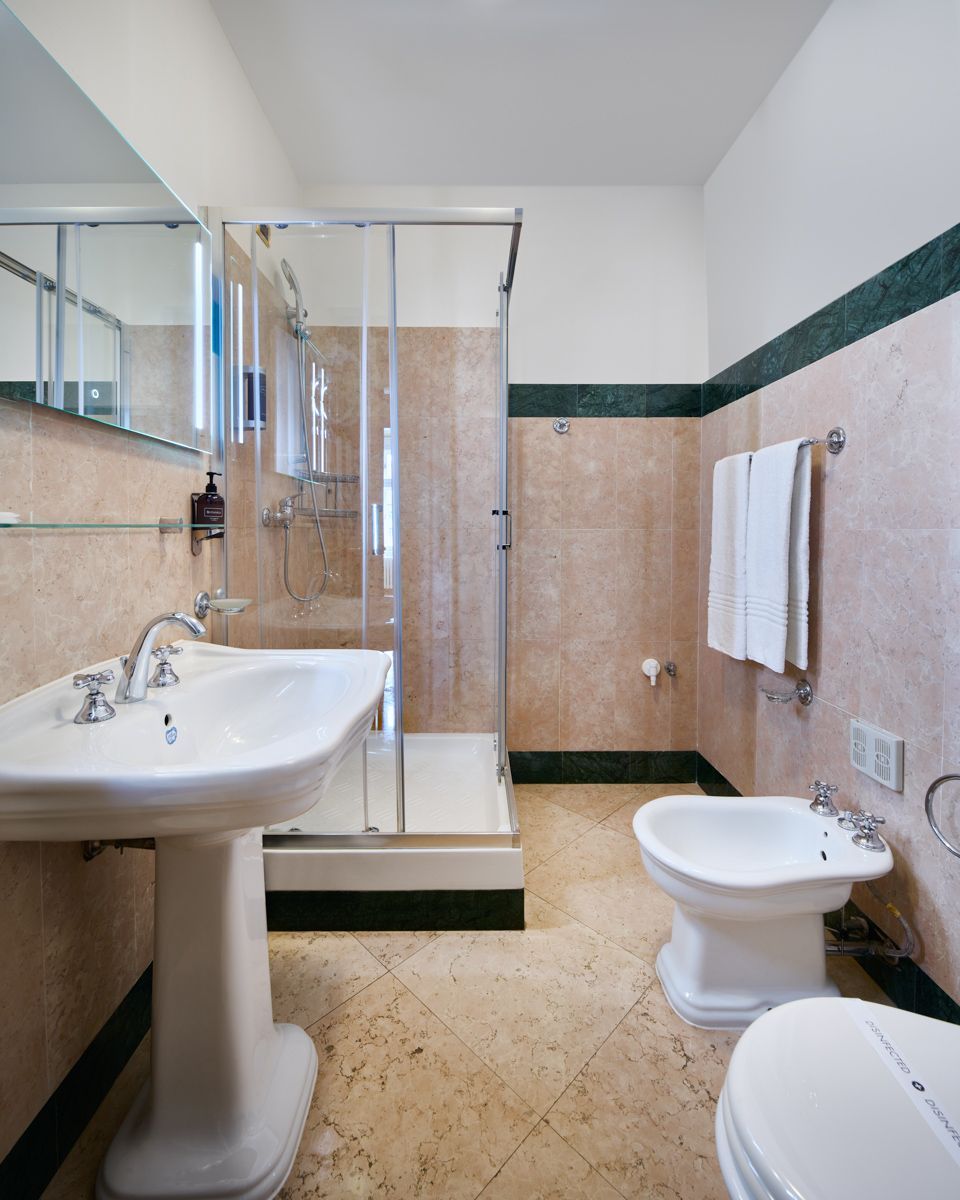 Badezimmer mit Waschtisch, Duschkabine, WC und Bidet. Pfirsichfarbene Wände, Marmorverkleidung und ein Spiegel.