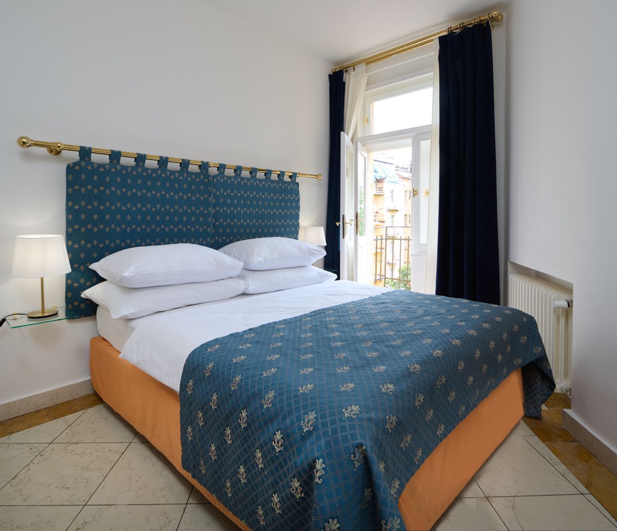 Schlafzimmer mit blauen und orangen Akzenten. Das Bett hat ein türkisfarbenes Kopfteil und eine türkisfarbene Tagesdecke. Fenster mit dunkelblauen Vorhängen.