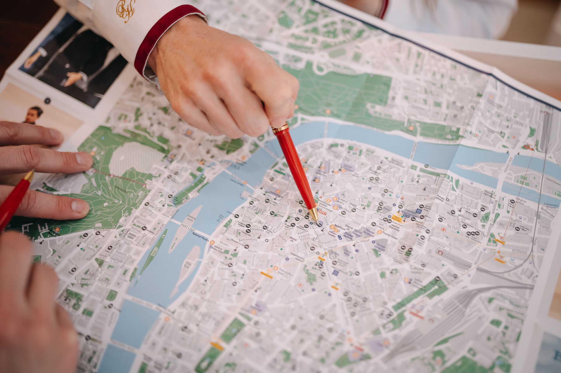 Hände zeigen auf einen Stadtplan mit roten Stiften, einem Fluss und Grünflächen.