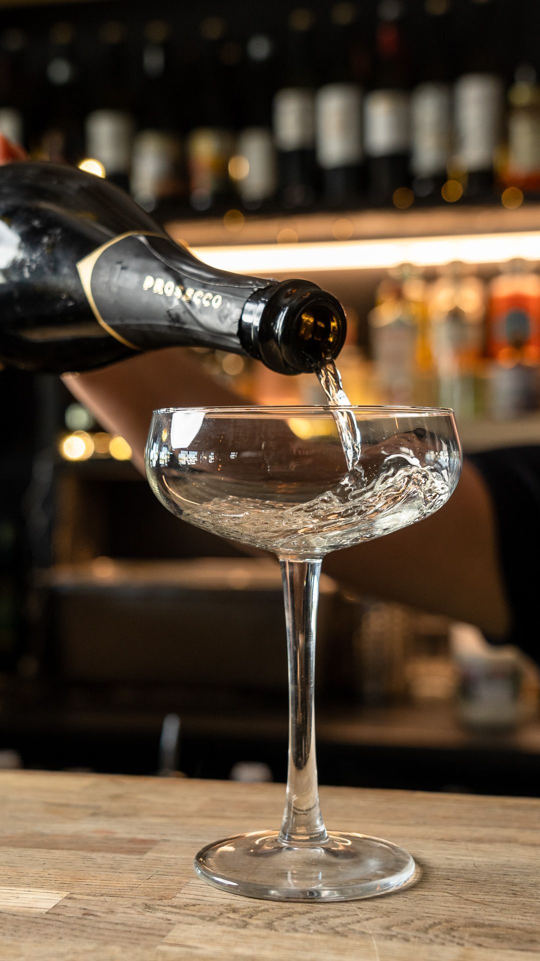 Champagne being poured into a stemmed coupe glass at a bar.