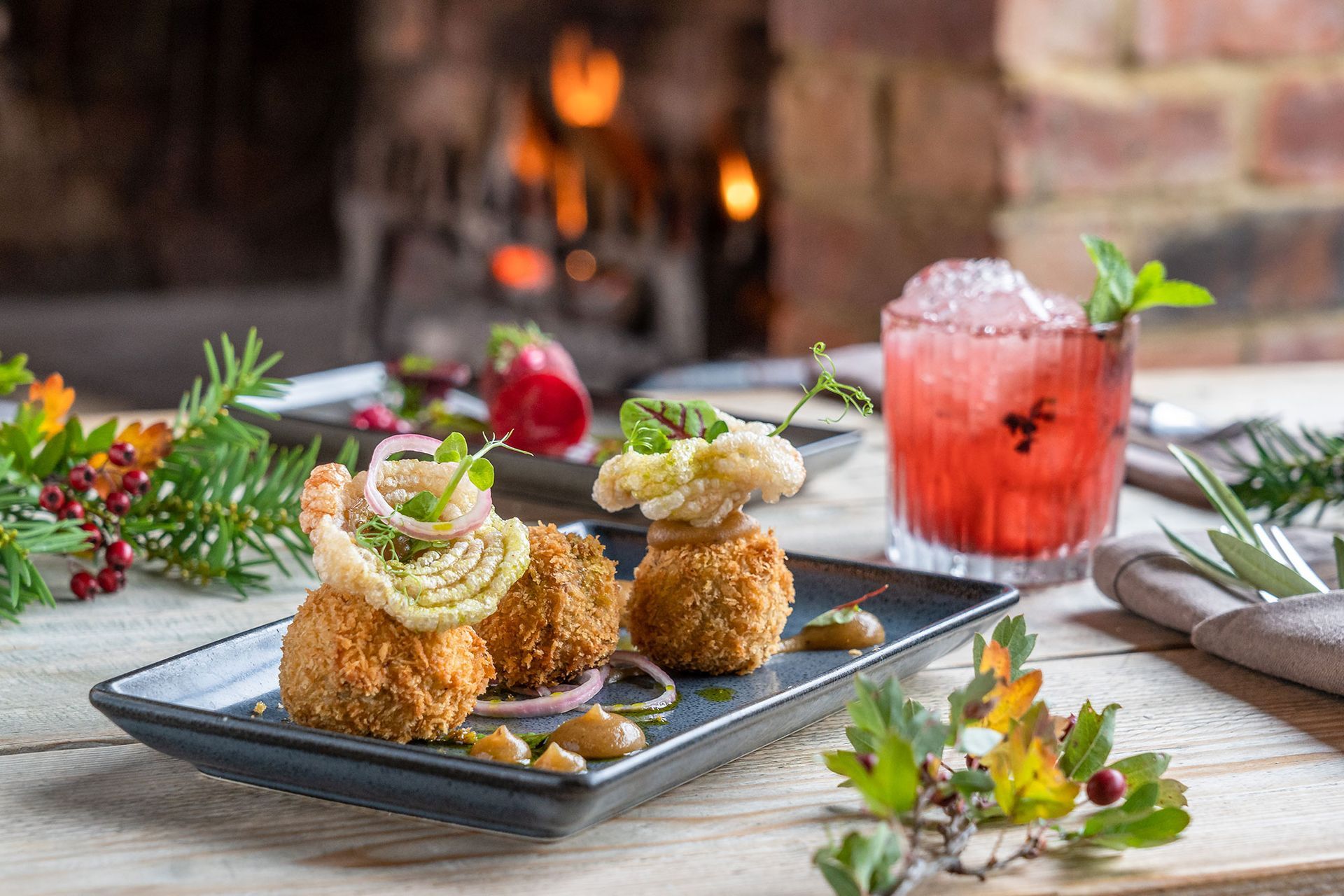 Appetizers and a cocktail on a table, with a fireplace in the background, festive decorations.